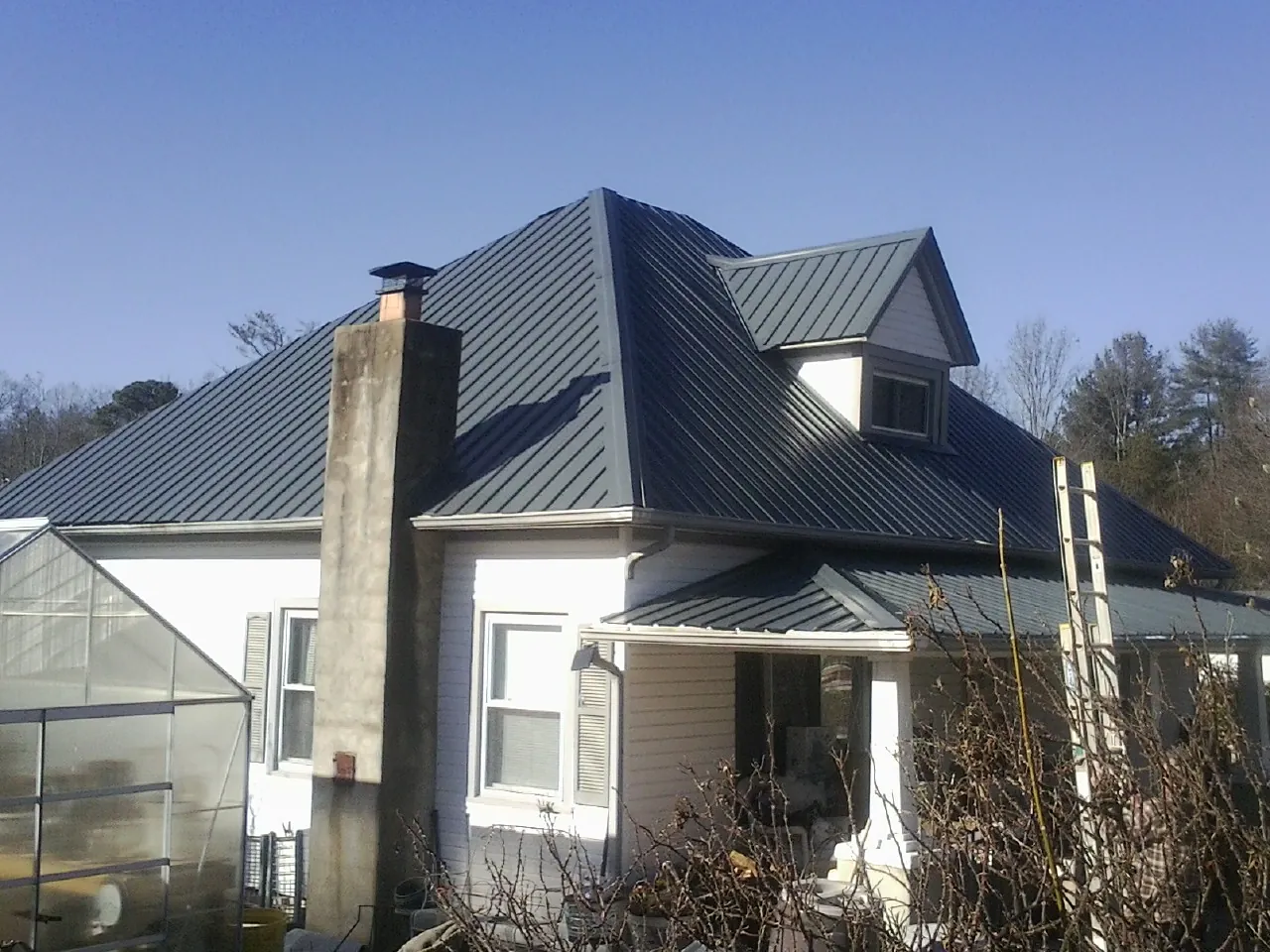 Dark blue standing seam metal roof on a white farmhouse with dormer — Slate & Tile Roof Repair by Roofing Brothers in Jericho