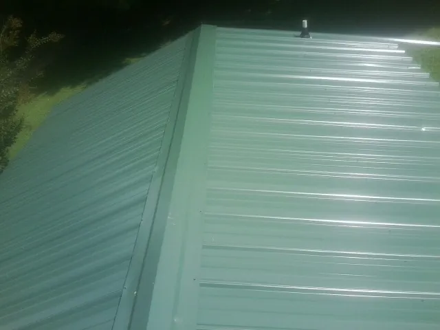New green metal panels meeting at the ridge of a roof — Flat Roof Repair work by our crew in Jericho