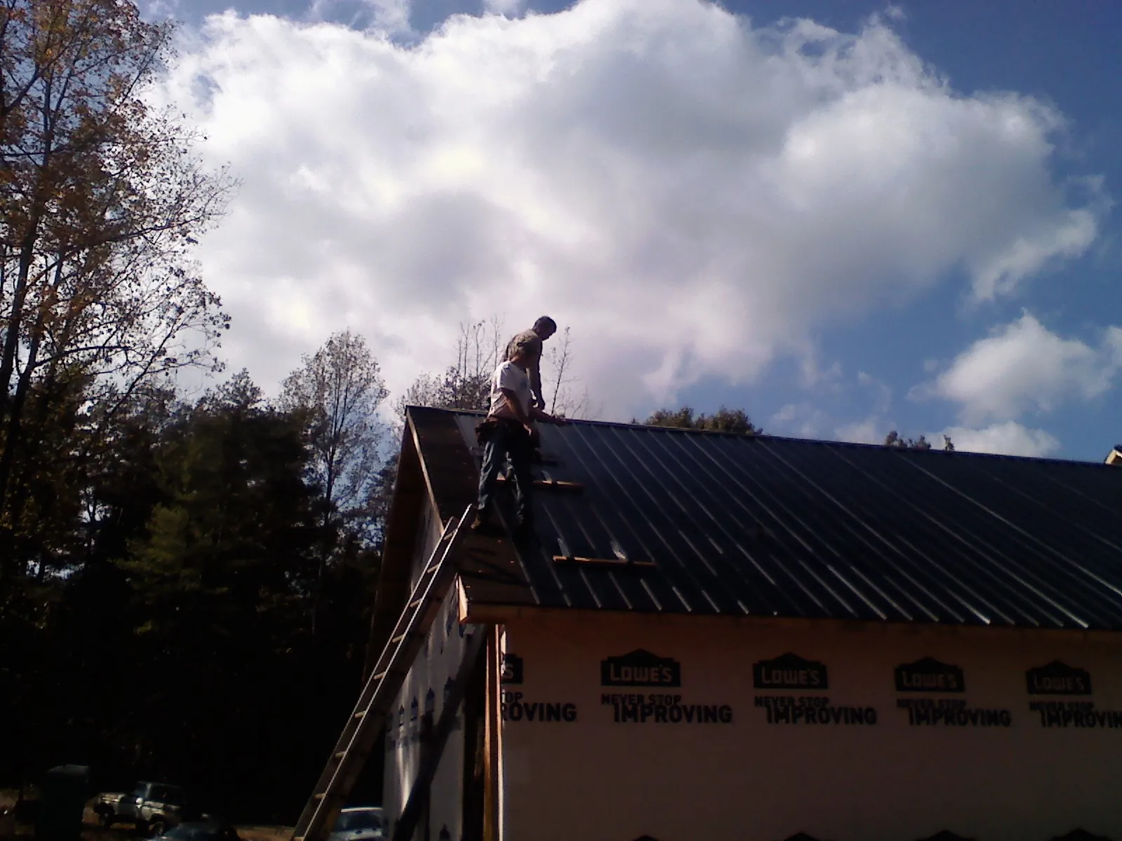 Roofer fastening dark metal panels high against a cloudy sky, from a Roof Inspection job in Jericho